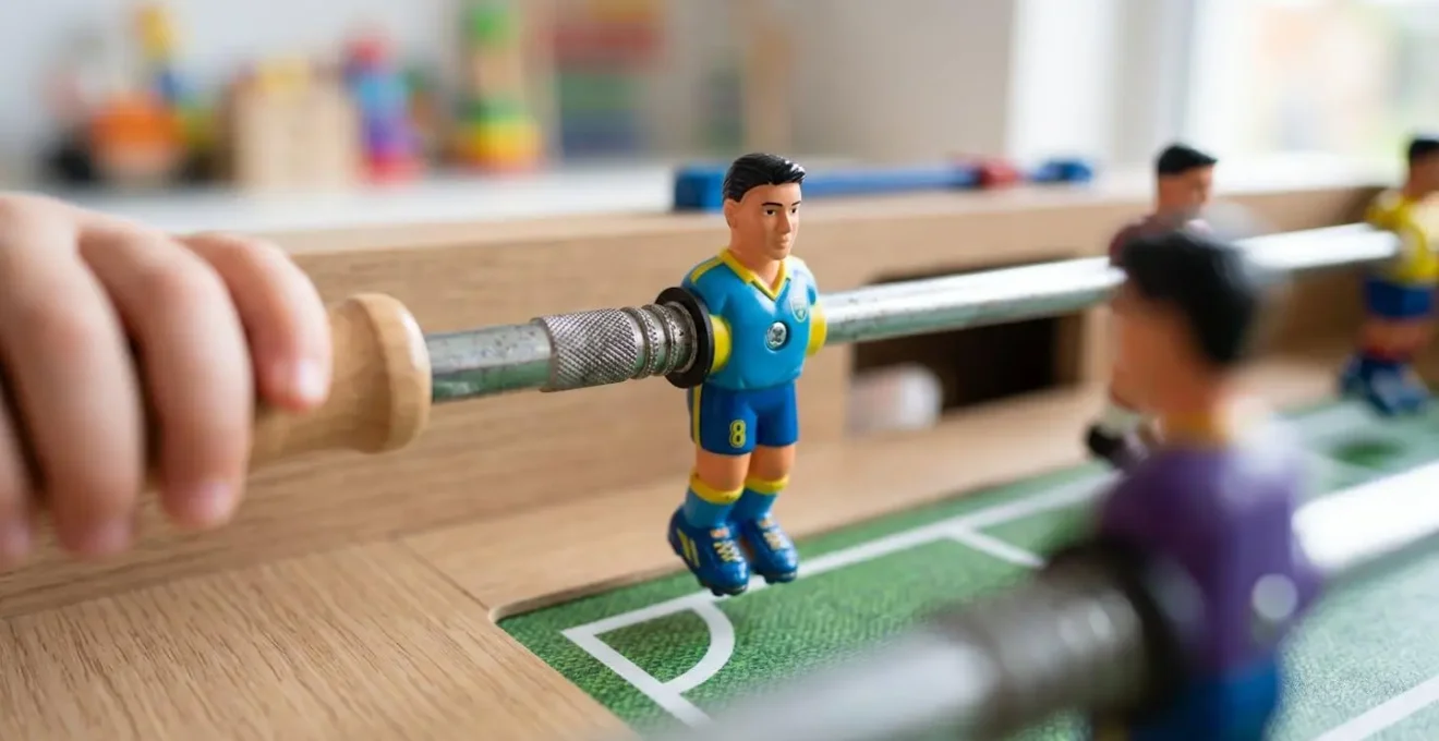 Gros plan sur un baby-foot au design contemporain et des playmobils colorés posés sur une surface en bois clair épuré, avec une lumière naturelle latérale créant un joli bokeh en arrière-plan